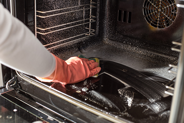 Cleaning the interior of an oven with a gloved hand and sponge.