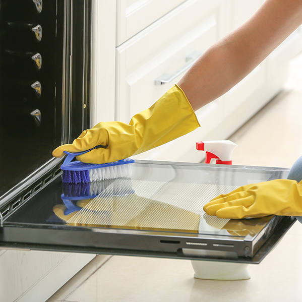 Cleaning an oven door panel with a brush and spray cleaner.